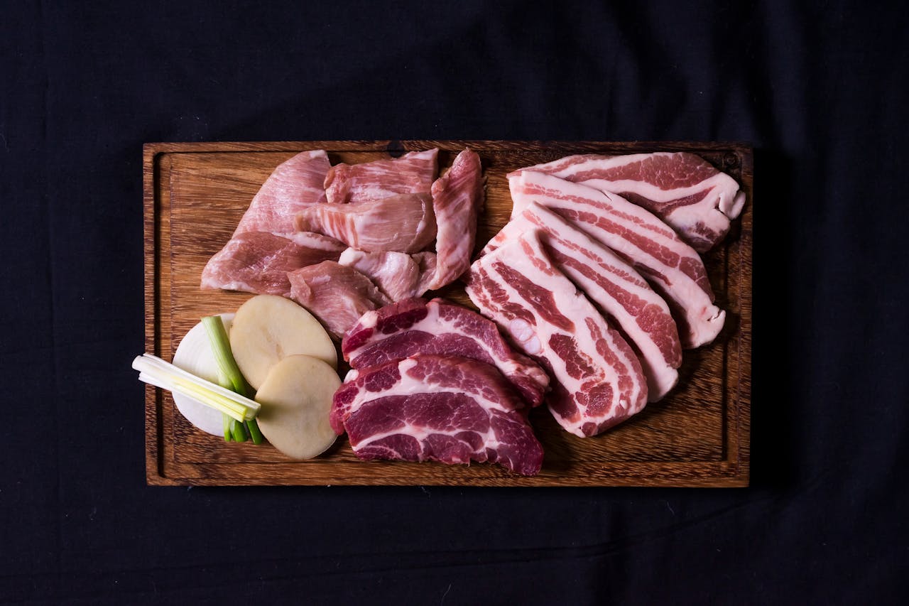 hero-img-01 Variety of raw pork cuts arranged on a wooden chopping board, ideal for cooking preparations.